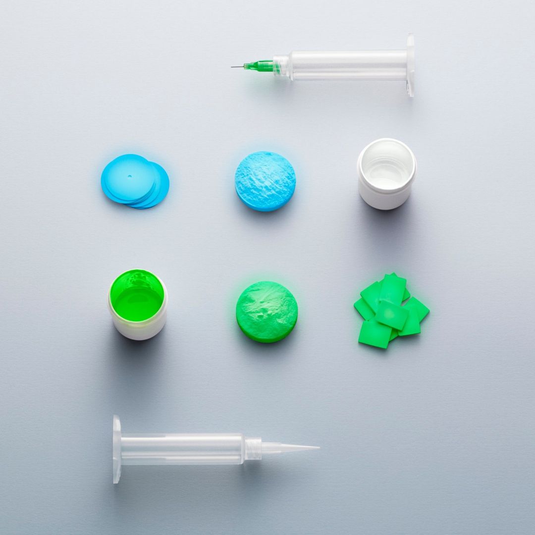 Overhead shot of two syringes, two containers of fluid, round blue fluid samples, a round green fluid sample, and green squares on a gray background.