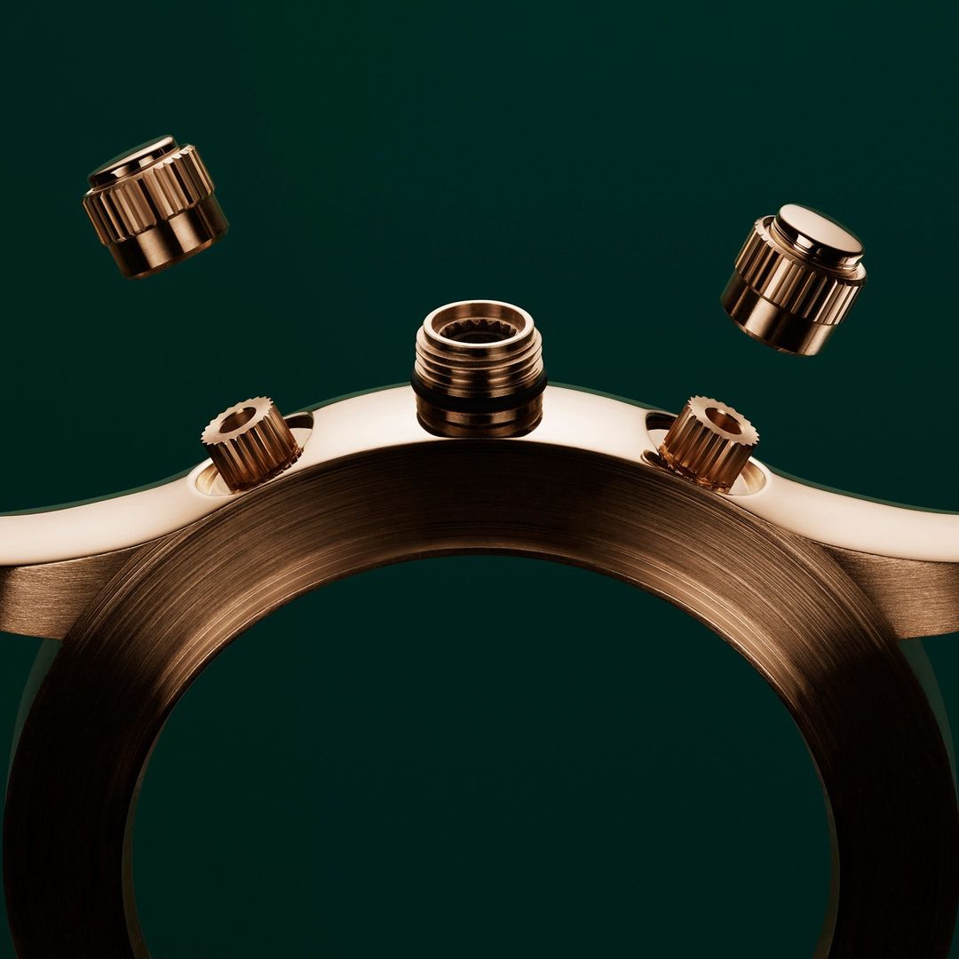 Macro shot of a rose gold watch casing with floating rose gold watch crowns against a dark green background, showcasing craftsmanship.