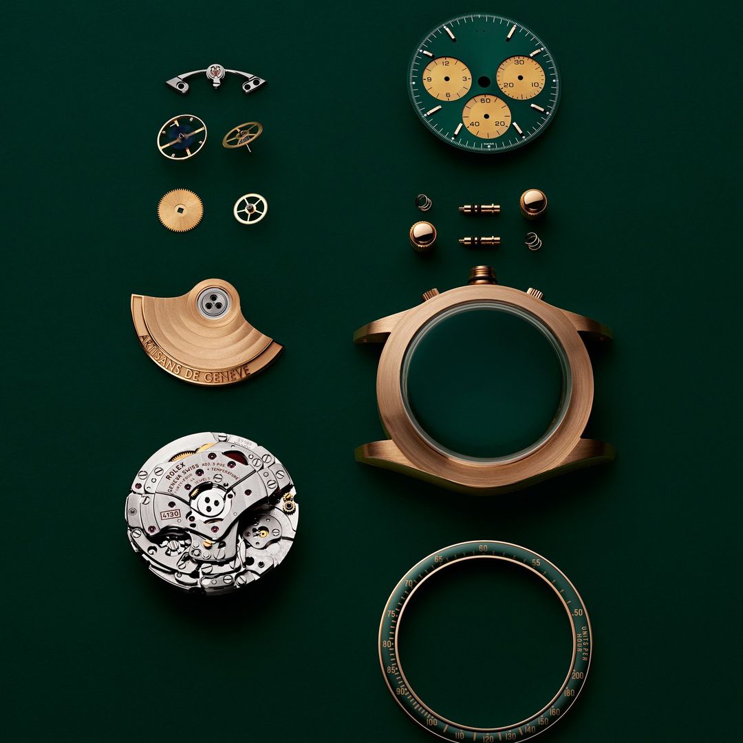 Watch components including face, casing, and gears are laid out on a dark green surface, displayed in an exploded view.