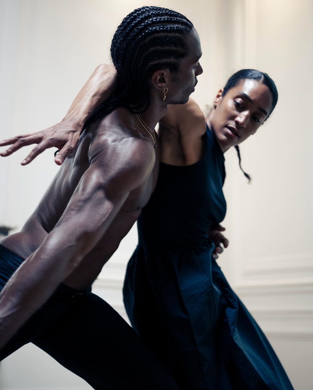Two athletic dancers, a man and woman, perform a modern dance routine in a bright, minimalist space with dramatic, expressive poses and dark clothing.