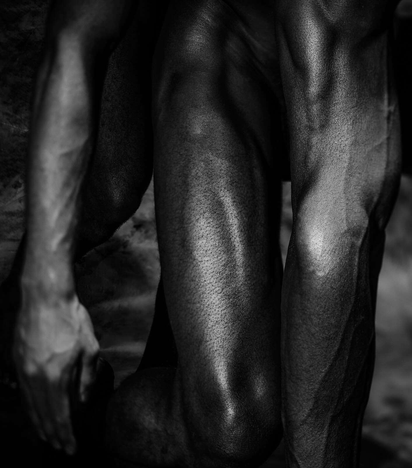 Monochromatic photograph showcasing the detailed musculature of a person's legs and arm with soft, diffused lighting on a dark background.