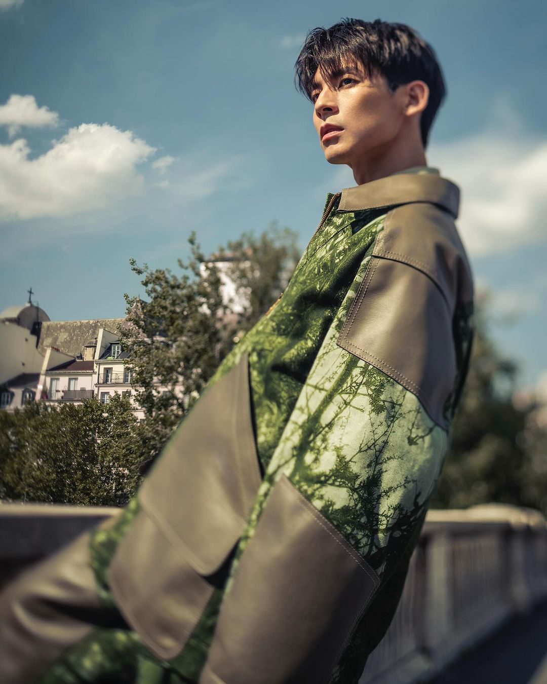 Portrait of a man in an olive green patterned jacket looking away against an outdoor sky and architectural background in Paris.
