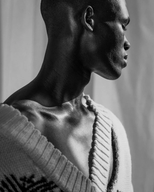 Monochrome portrait of an adult male wearing a patterned sweater, showcasing a close-up of his face in profile against a bright background.