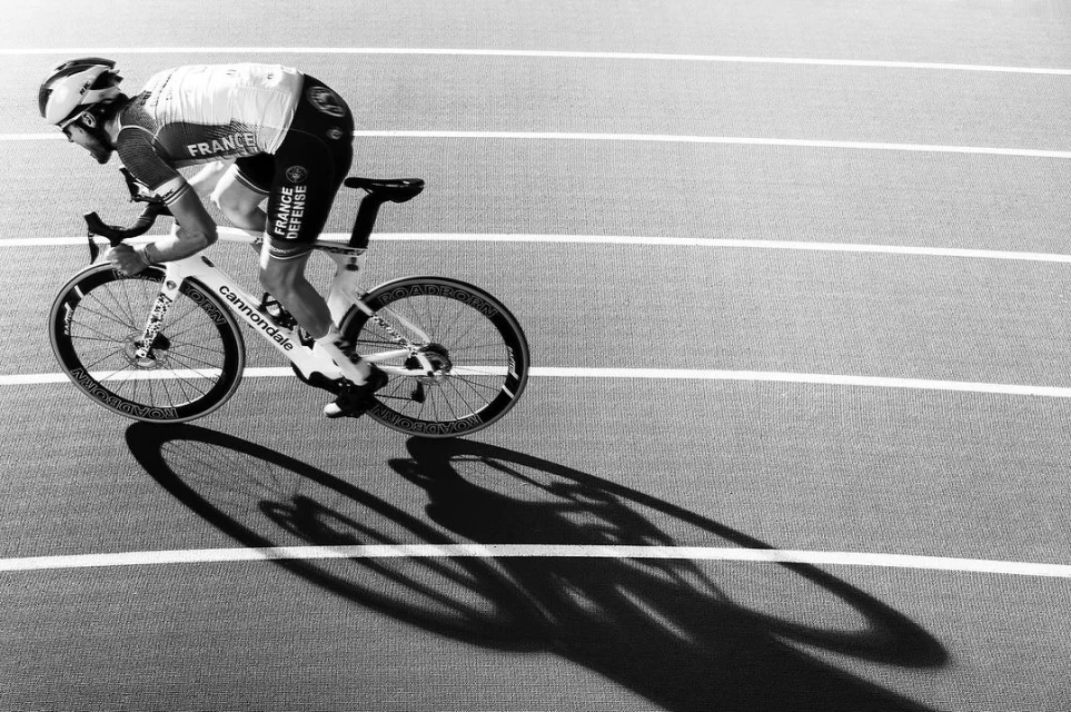 Cyclist in white jersey and black shorts on a Cannondale bike, riding on a running track in a monochromatic image with hard shadows.