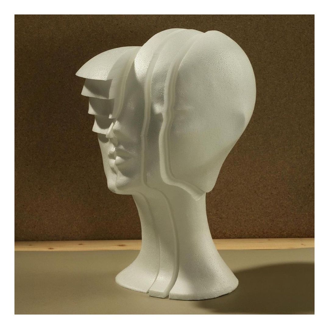 Sliced styrofoam human head sculpture on a beige surface against a tan background, creating a visually intriguing art piece.