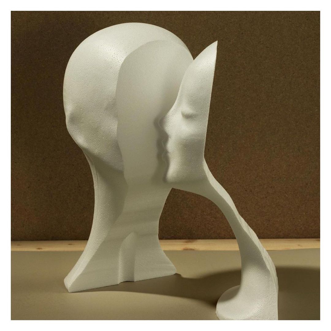 Sculptural still life showcases a white foam head with smooth texture and abstract facial features, set against a brown and tan background.