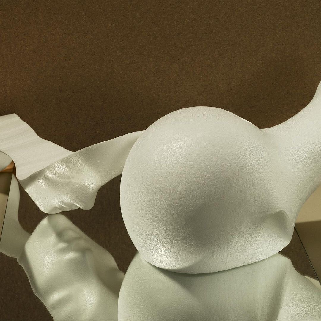 Close-up of an abstract, white sculptural object with a draped fabric on a reflective surface against a textured brown background.