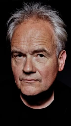 Close-up portrait of an older man with short grey hair and a serious expression against a dark background