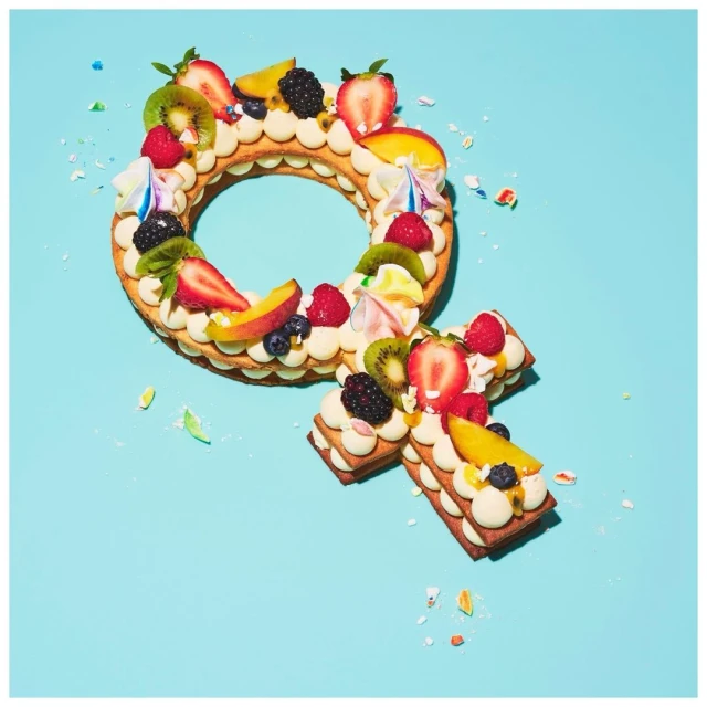 Overhead shot of female symbol-shaped dessert made with pastry cream, fresh fruit, cake, and light blue background.