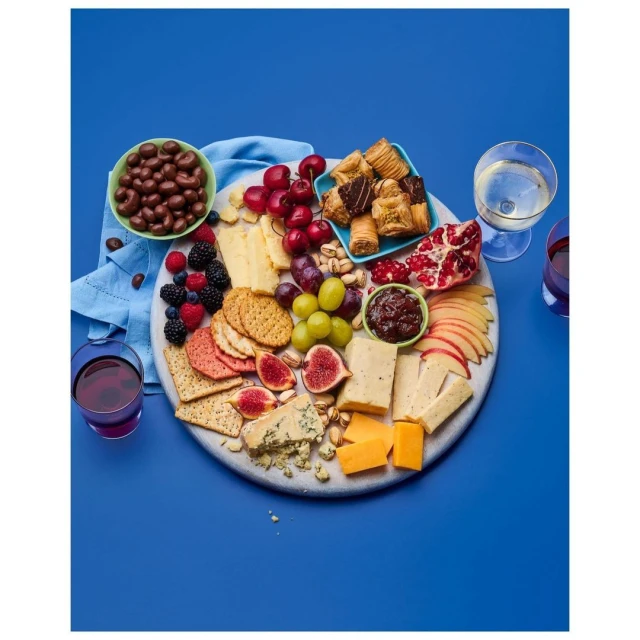 Overhead shot of a charcuterie board featuring cheese, fruit, crackers, pastries, and nuts, accompanied by glasses of red and white wine.