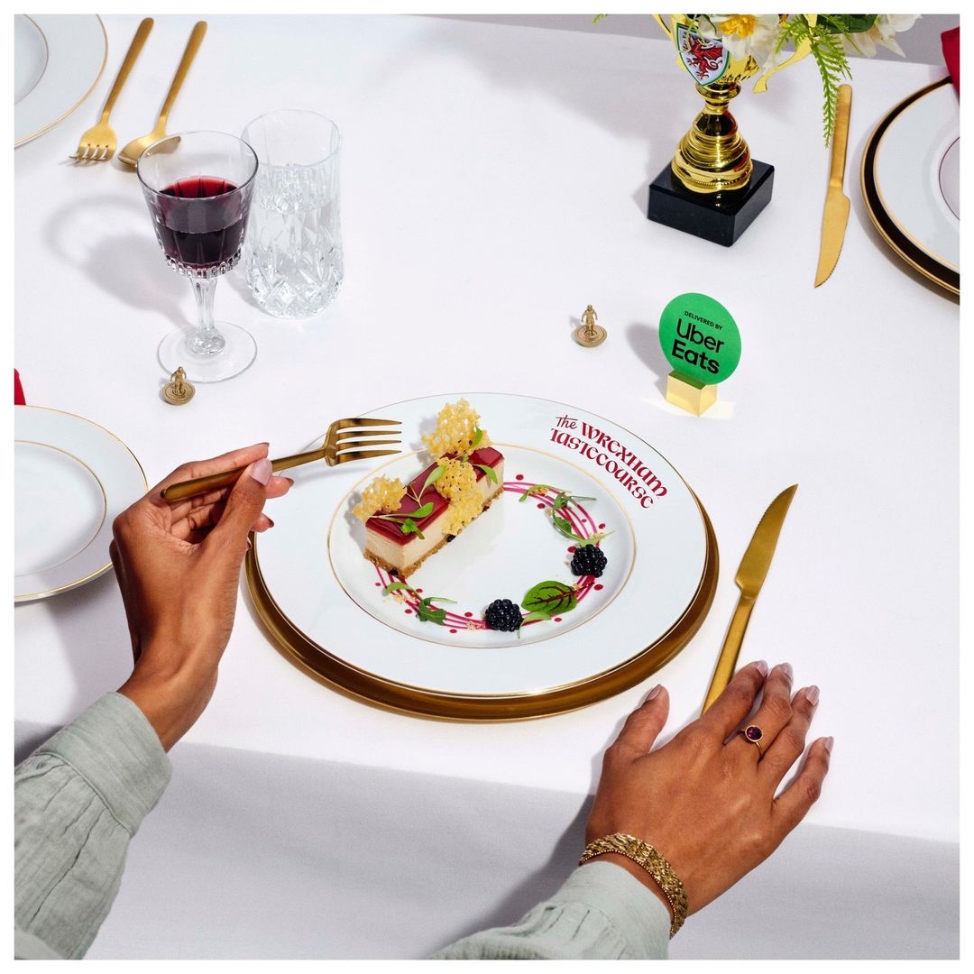 Close-up of diner's hands using a gold fork to take a bite of dessert on a white plate with a gold rim at a table setting.