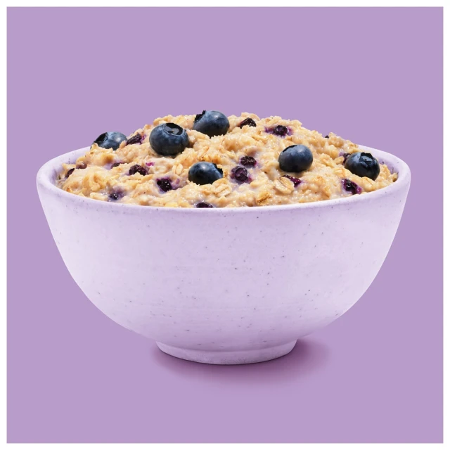 Close-up of a ceramic bowl filled with oatmeal and fresh blueberries against a solid purple background in a studio setting.