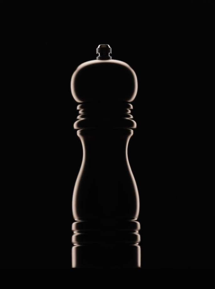 Elegant studio shot of a sleek, dark-toned pepper grinder against a stark black background, highlighted with rim lighting.