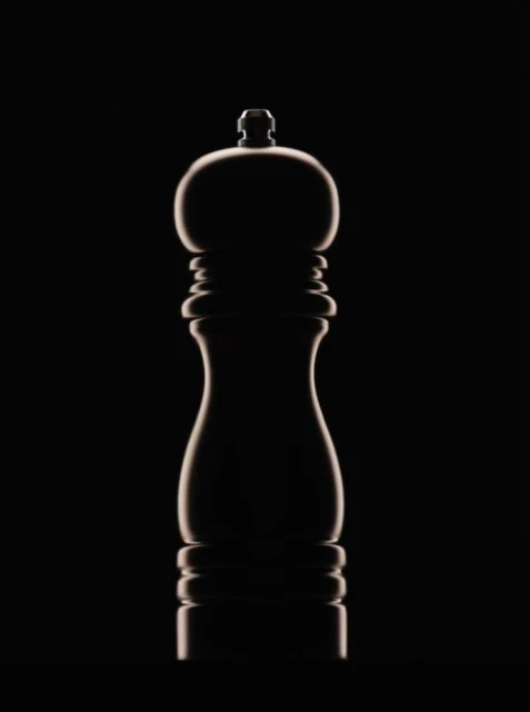 Elegant studio shot of a sleek, dark-toned pepper grinder against a stark black background, highlighted with rim lighting.