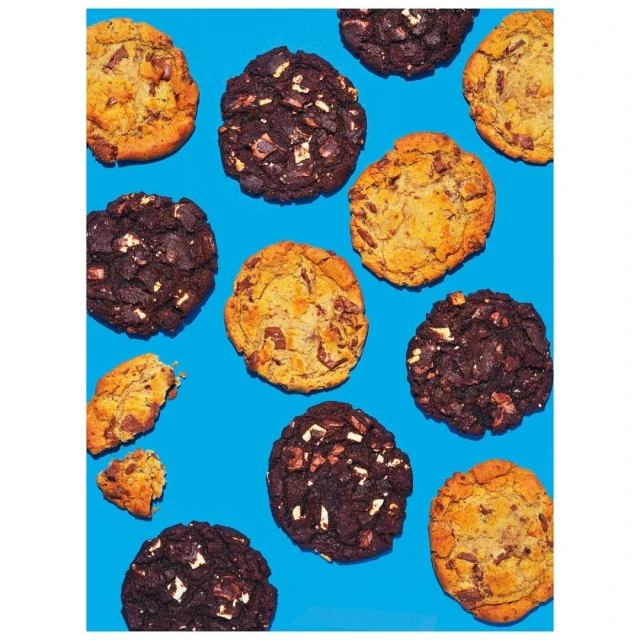 Overhead shot of assorted dark chocolate and blond chocolate chip cookies arranged on a bright blue background, food photography.