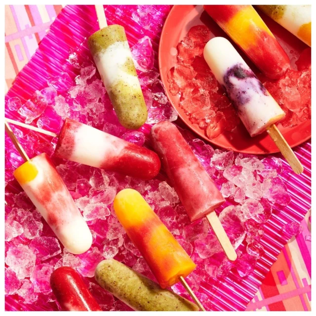 Assorted colorful popsicles on a pink plate of crushed ice and a pink background create a summery food and beverage still life.