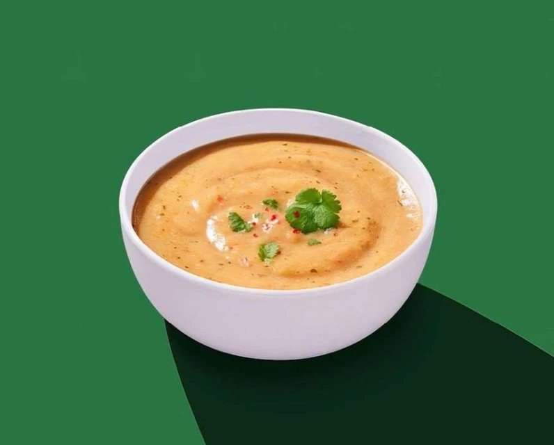 Overhead shot of a bowl of creamy soup garnished with herbs and red pepper flakes on a green background with a dark shadow.