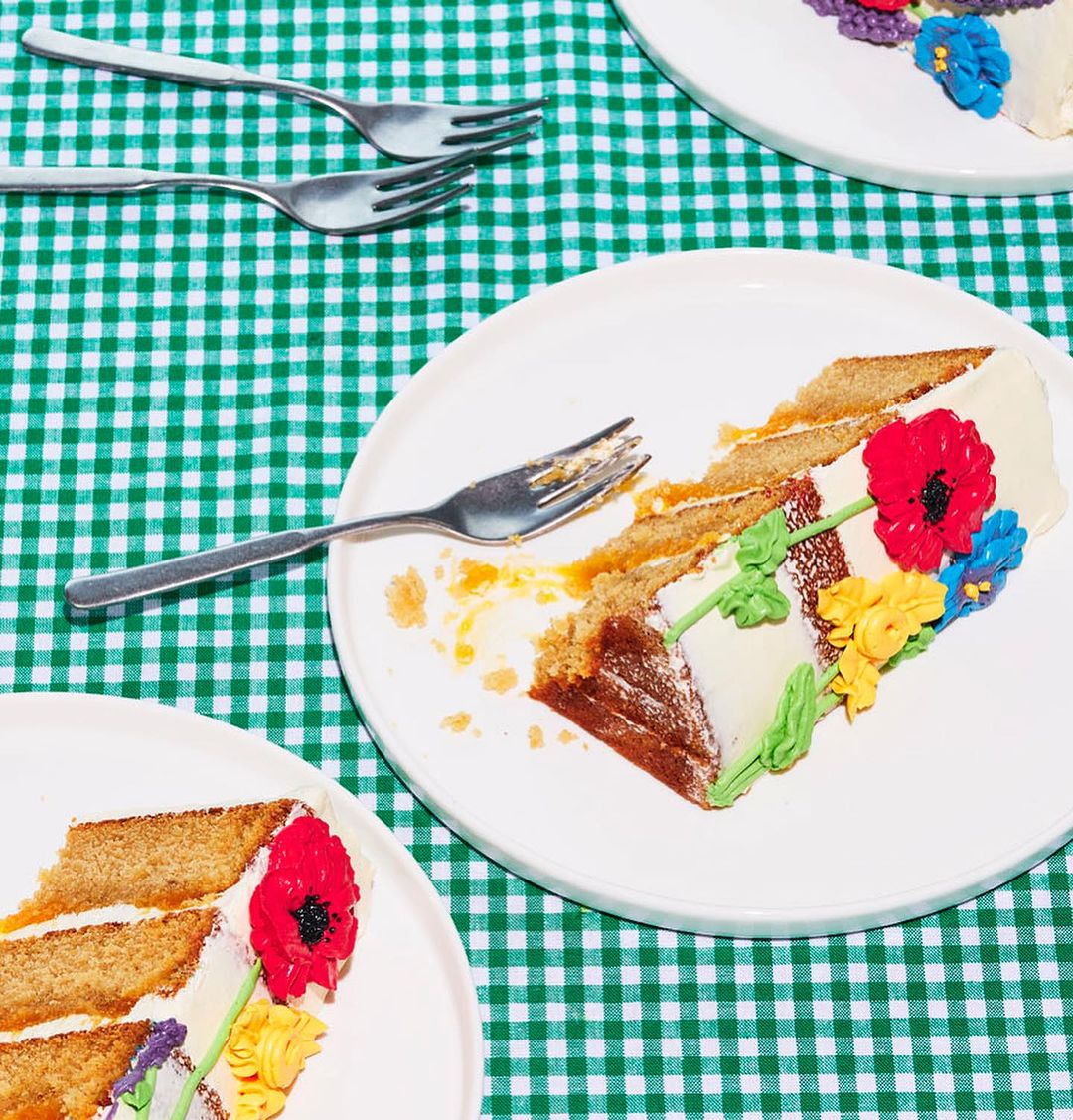 Overhead shot of cake slices with floral frosting on plates with forks, arranged on a green and white checkered tablecloth.