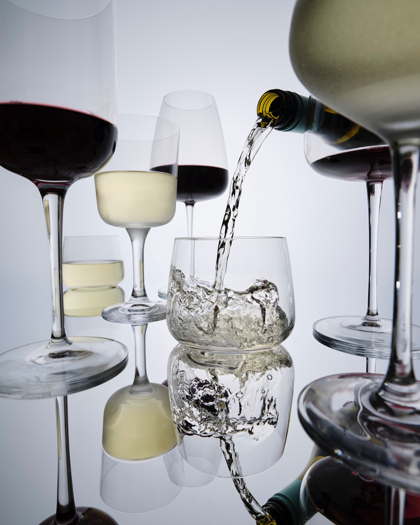 Wine bottle pouring liquid into glass among glasses of red and white wine on a reflective surface against a gradient background.