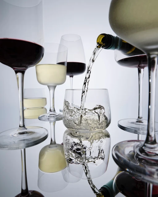 Wine bottle pouring liquid into glass among glasses of red and white wine on a reflective surface against a gradient background.