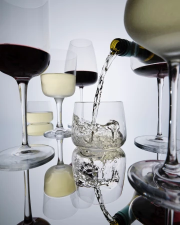 Wine bottle pouring liquid into glass among glasses of red and white wine on a reflective surface against a gradient background.