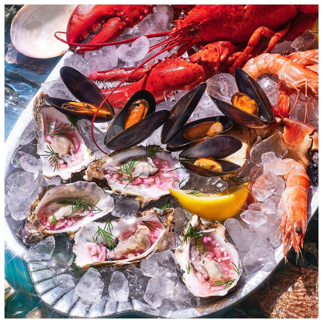 Overhead shot of raw oysters, mussels, lobster, and shrimp served on crushed ice on a silver platter for a seafood display.