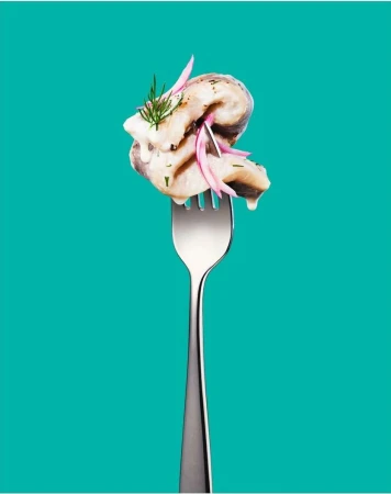 Close-up of marinated herring on a fork with dill and sliced red onion against a vibrant turquoise background, studio lighting.