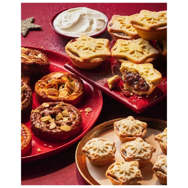 Festive dessert arrangement: star-topped mince pies and almond tarts elegantly displayed on red and gold-rimmed plates with white cream.