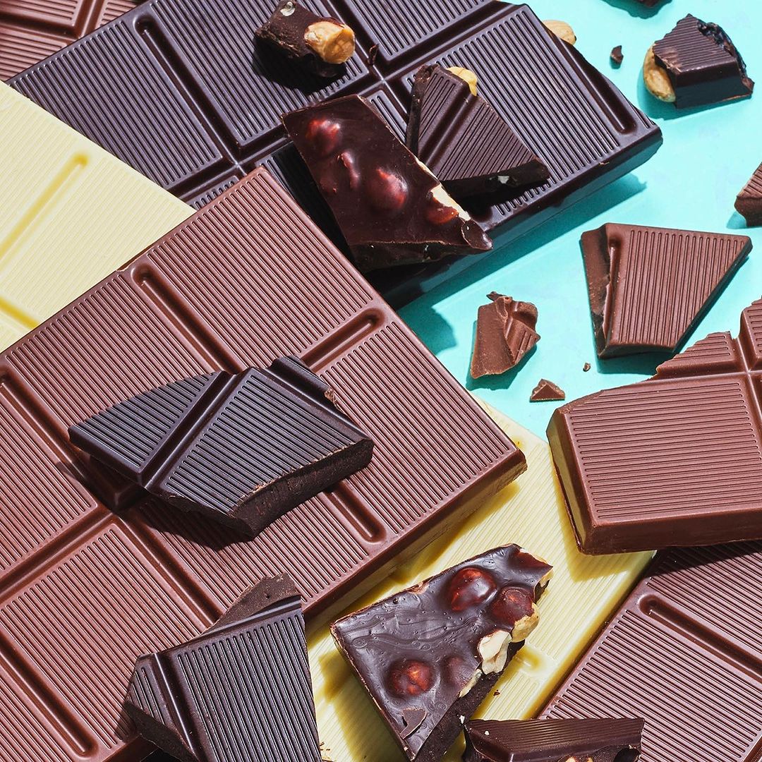 Assorted chocolate bars on a bright background. Dark, milk, and white chocolate pieces, some with nuts. Flat lay, overhead studio shot.