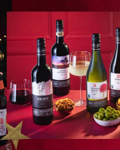 Arrangement of wine bottles, various appetizers, and glassware on a red surface against a red background, suggesting an elegant gathering.