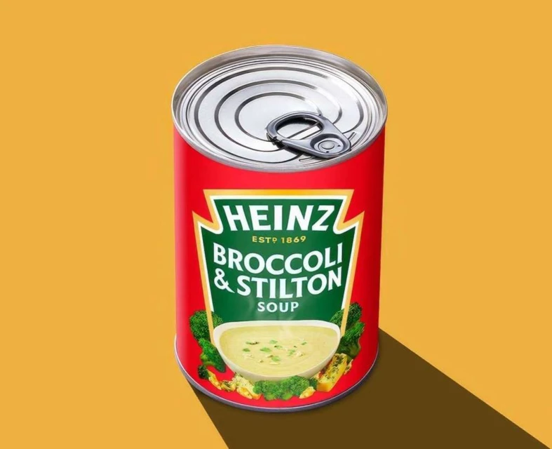 Heinz Broccoli & Stilton soup can on a yellow background with visible shadow. Food and beverage product shot with studio lighting.