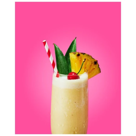 Tall glass filled with a tropical smoothie garnished with pineapple, a maraschino cherry, and a red and white straw, set against a bright pink background.