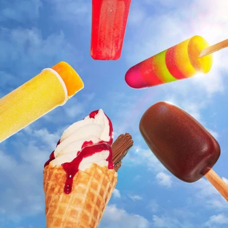 Low angle view of assorted colorful popsicles and ice cream cone against a bright blue sky with soft white clouds and sunlight.