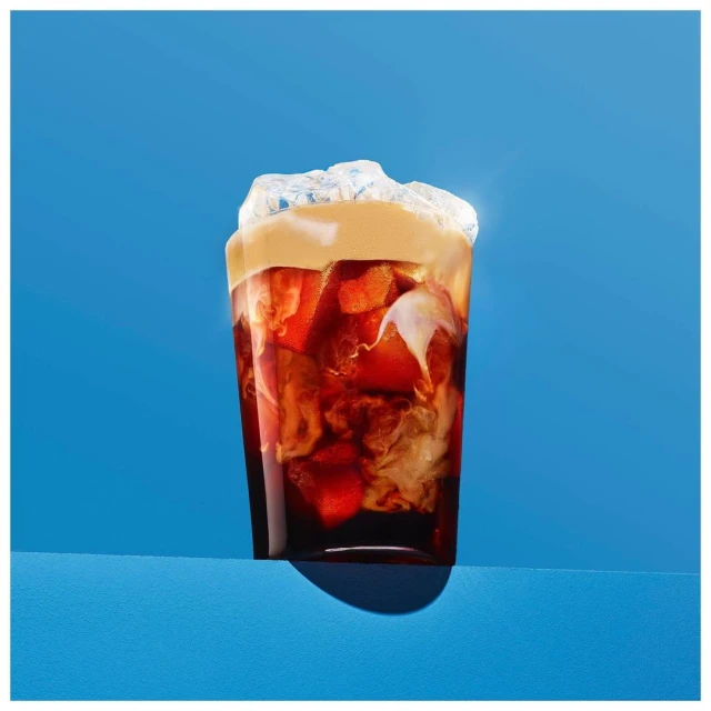 Iced coffee in a glass with milk and ice cubes against a blue background. Refreshing drink for summer enjoyment and caffeine boost.