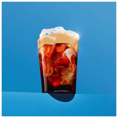 Iced coffee in a glass with milk and ice cubes against a blue background. Refreshing drink for summer enjoyment and caffeine boost.