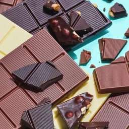 Overhead food photography by Frankie Turner featuring broken dark, milk, and white chocolate bars on a bright turquoise background.
