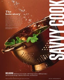 Copper colander with fresh green leaves and splashing water droplets against a warm brown background
