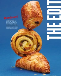 A vertical stack of three pastries including a pain au chocolat, a pain aux raisins, and a croissant against a vibrant blue background