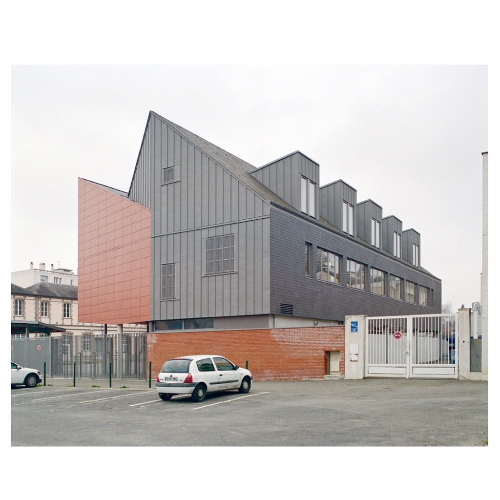 Exterior daytime shot of a contemporary building with gray cladding and a car parked in the asphalt parking lot.