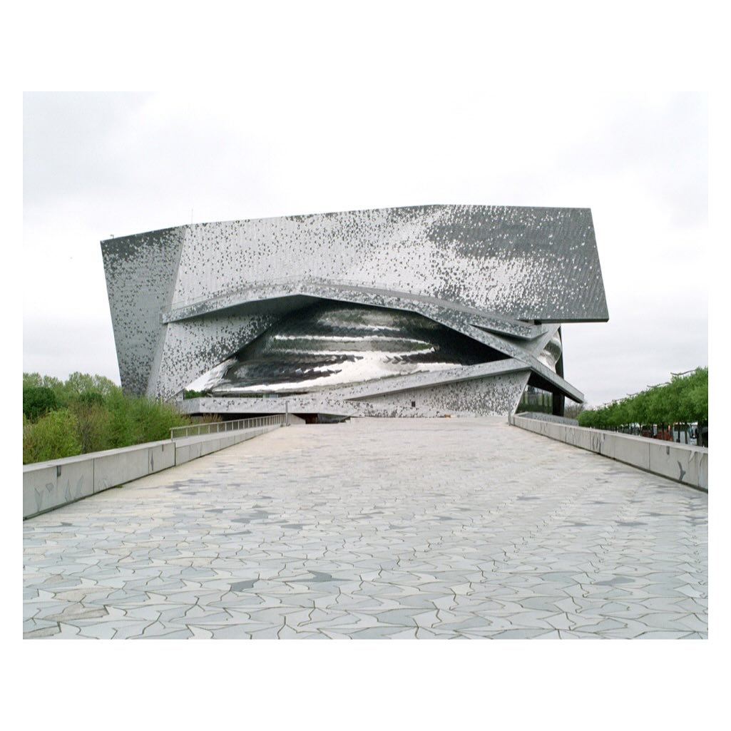 Exterior view of the Philharmonie de Paris, a modern concert hall with unique geometric design, seen on a cloudy day from the pedestrian bridge.