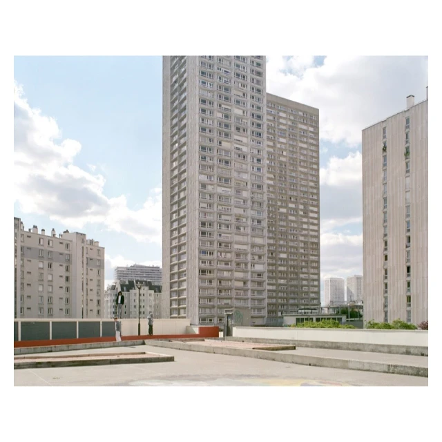 Urban landscape featuring concrete rooftops and tall apartment buildings under a cloudy sky, capturing city architecture.