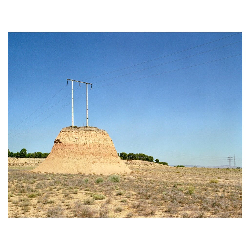 Unusual view of power lines atop an eroding mesa in a desolate landscape against a clear blue sky, creating a starkly beautiful scene.