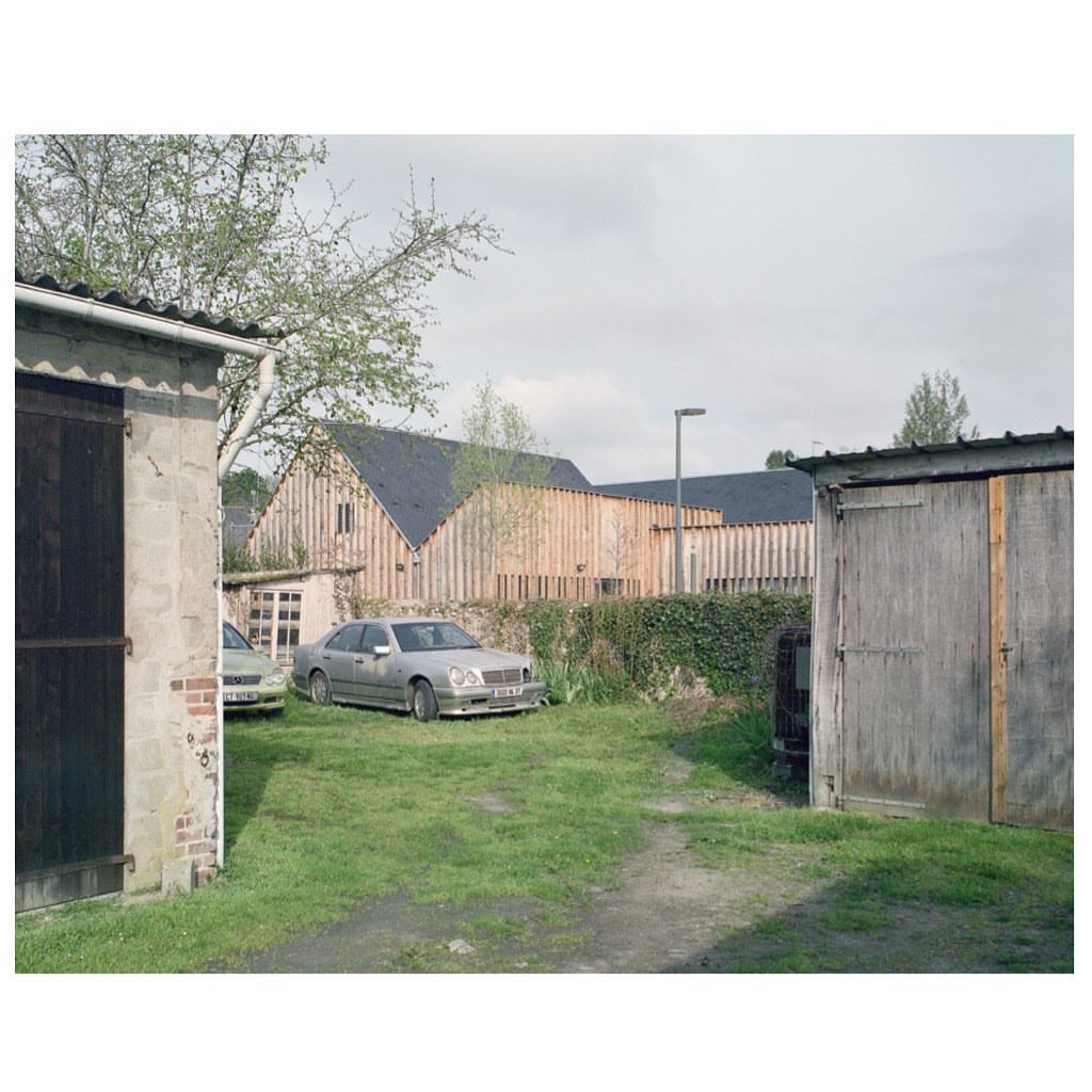 Two vintage Mercedes-Benz cars sit on a green lawn near buildings, garages, and trees under a cloudy sky in a daytime outdoor setting.