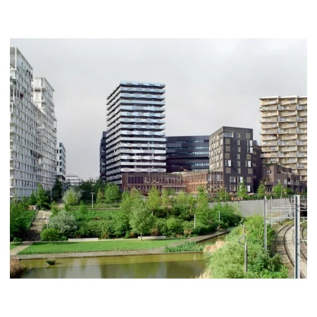Modern urban landscape featuring contemporary architecture, a reflective water feature, and lush greenery on an overcast day.