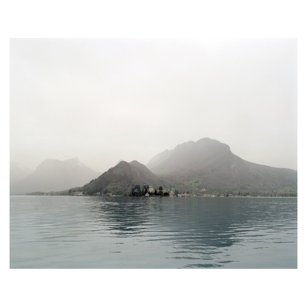 Scenic view of a calm lake with castle in the background and mist-covered mountains, creating a tranquil and picturesque landscape.