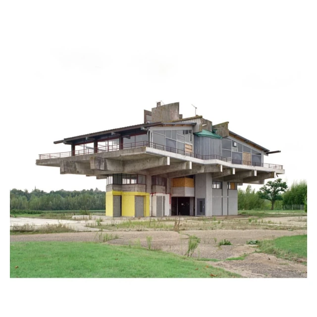 Exterior view of a unique concrete architecture with large overhanging balcony surrounded by grassy fields and a grey sky.