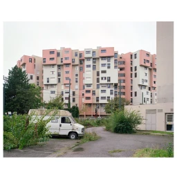 Exterior shot of a pink and white apartment building in Paris with a white parked van in the foreground by Fred Guillaud.