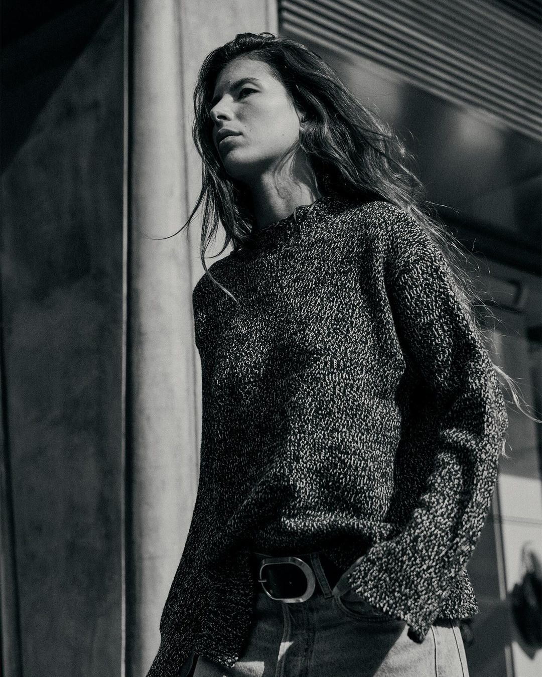 Monochrome low-angle portrait of a woman in a textured knit sweater and jeans standing outdoors in Paris.