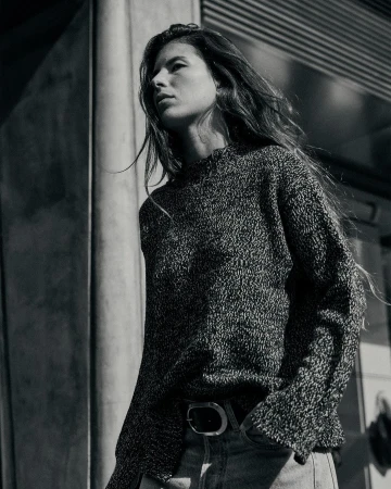 Monochrome low-angle portrait of a woman in a textured knit sweater and jeans standing outdoors in Paris.