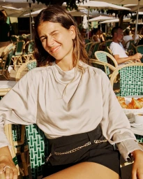 Young woman in a silk blouse winking at a café table in Paris by photographer Fred Meylan.